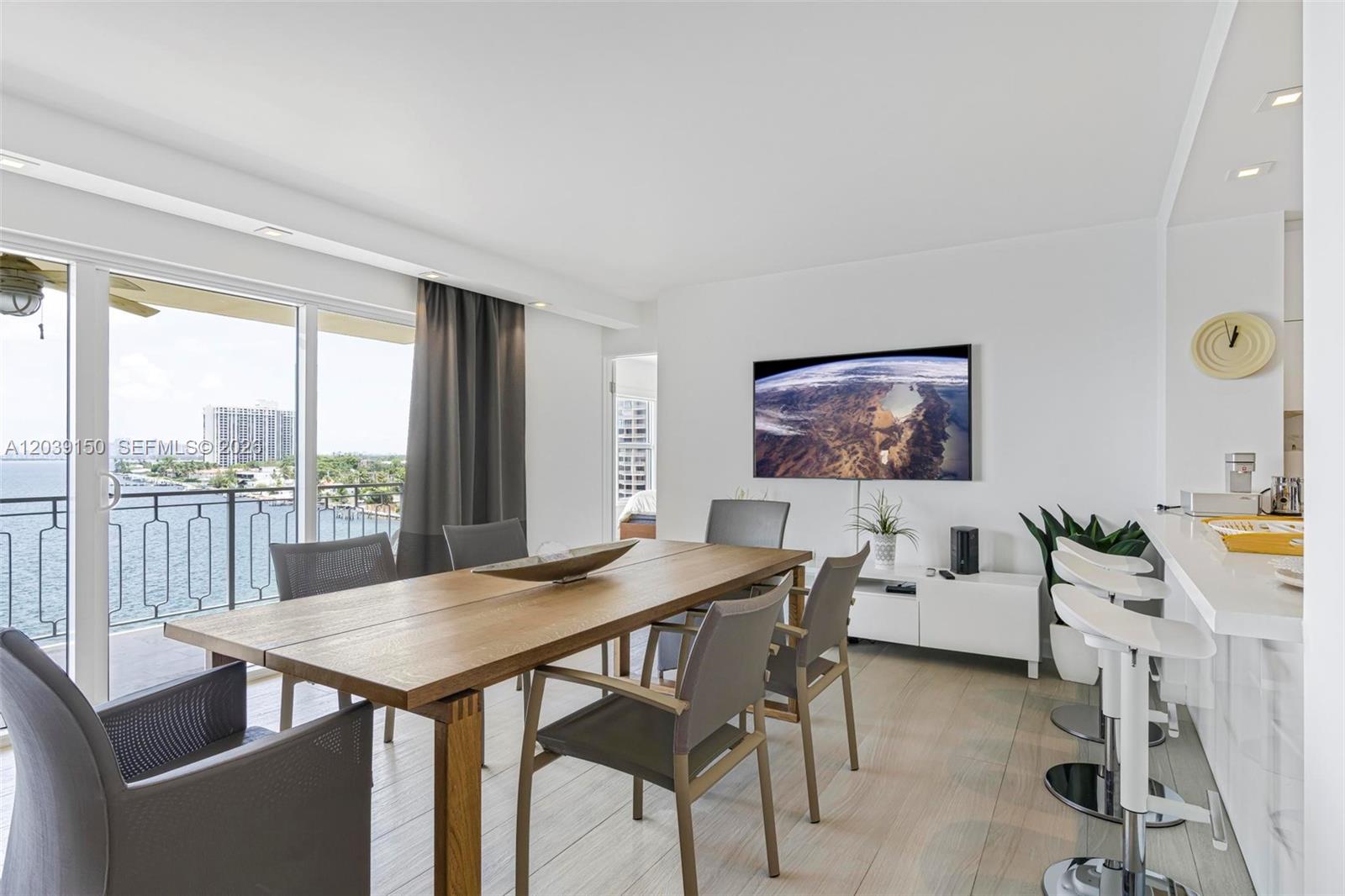 A dining area with a wooden table, grey chairs, and a balcony overlooking the water — 11111 Biscayne Blvd # 8C, Miami FL 33181, MIAMI, FL