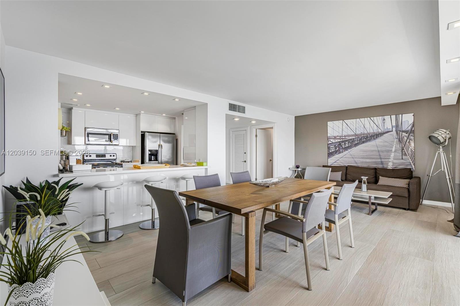 An open-concept living and dining area features a kitchen with white cabinetry and wood flooring — 11111 Biscayne Blvd # 8C, Miami FL 33181, MIAMI, FL