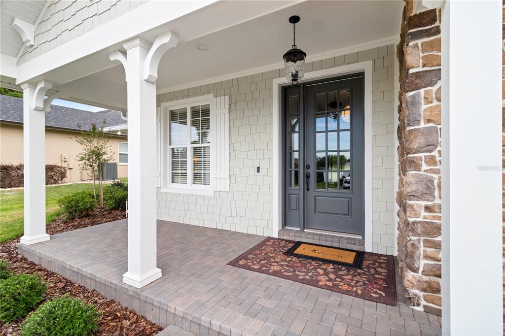 A covered front porch features a gray door, stone siding, and a brick paver floor — 2229 COACHMAN LOOP, LAKELAND, FL