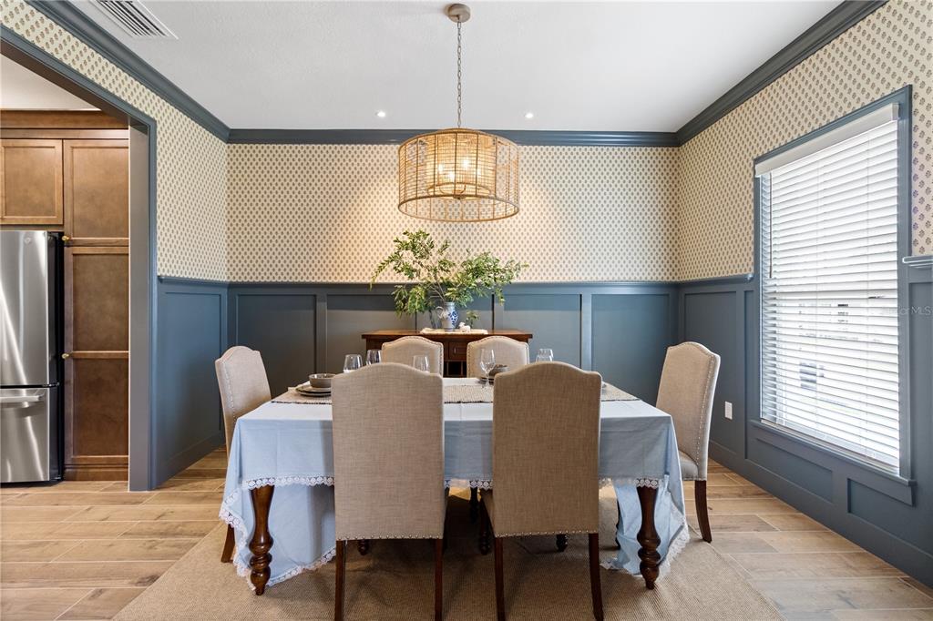 A dining room features blue wainscoting, patterned wallpaper, a drum pendant light, and upholstered chairs — 2229 COACHMAN LOOP, LAKELAND, FL