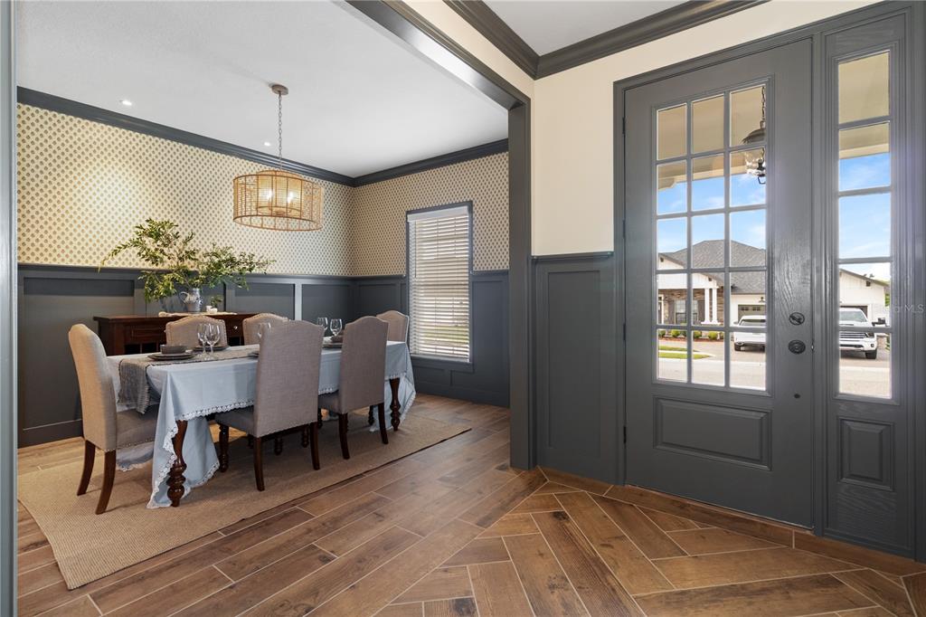 A dining room with patterned wallpaper and wainscoting sits beside a gray front entryway door — 2229 COACHMAN LOOP, LAKELAND, FL