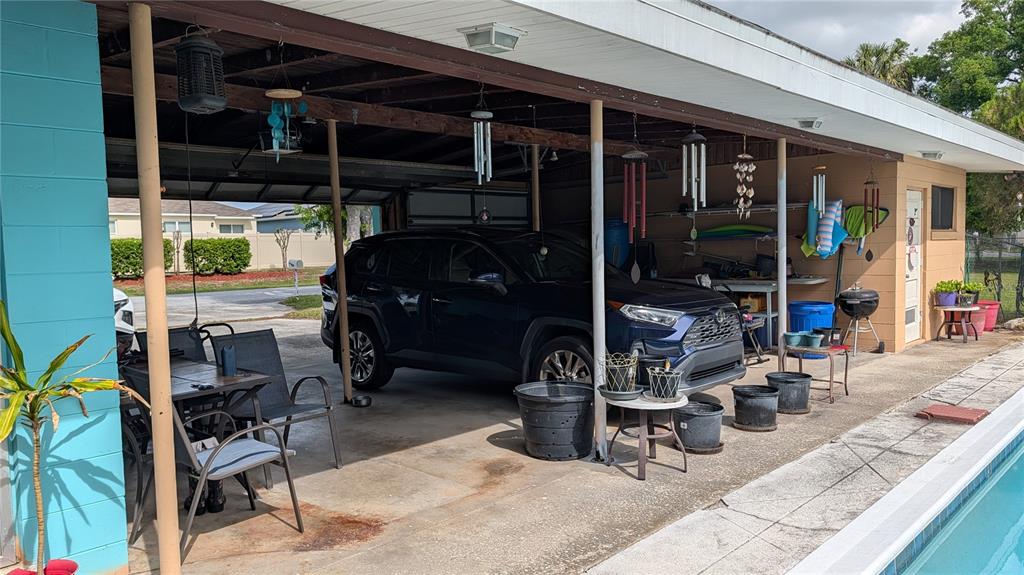 A covered carport features a parked SUV, outdoor seating, potted plants, and hanging wind chimes — 1619 PEARCE ROAD NW, WINTER HAVEN, FL