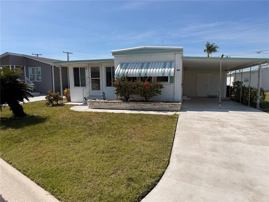 A single-story manufactured home with a white exterior, striped window awning, and attached carport — 315 PEACE MANOR, PALMETTO, FL