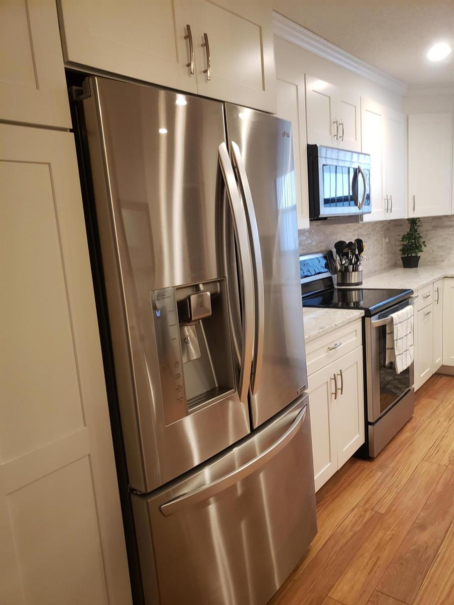 A kitchen features stainless steel appliances, white cabinetry, and light-colored countertops with wood flooring — 6021 SE Landing Way Bldg 2 Unit #2 Bldg 2, Stuart FL 34997, STUART, FL