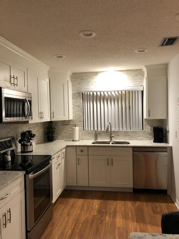 A kitchen features white cabinets, stainless steel appliances, a stone backsplash, and wood-look flooring — 6021 SE Landing Way Bldg 2 Unit #2 Bldg 2, Stuart FL 34997, STUART, FL