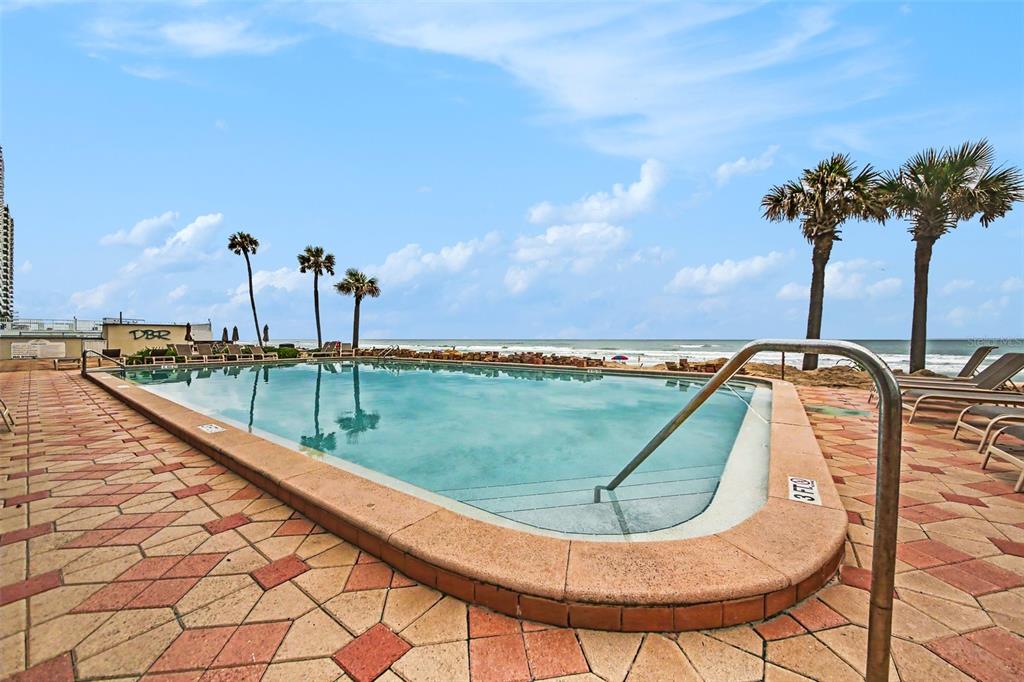 A rectangular swimming pool overlooks the ocean with palm trees and lounge chairs nearby — 2700 N ATLANTIC AVENUE UNIT 214, DAYTONA BEACH, FL