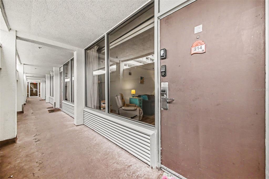 A brown apartment door with a number sign sits beside a large exterior window — 2700 N ATLANTIC AVENUE UNIT 214, DAYTONA BEACH, FL