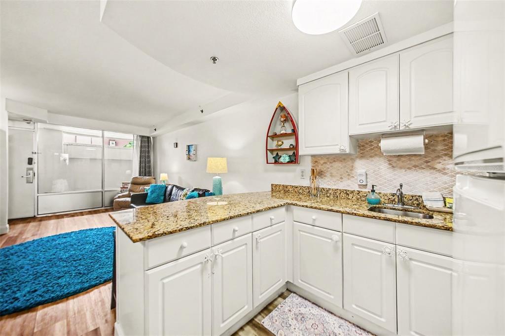 A kitchen with white cabinets and granite countertops overlooks a living area with wood flooring — 2700 N ATLANTIC AVENUE UNIT 214, DAYTONA BEACH, FL