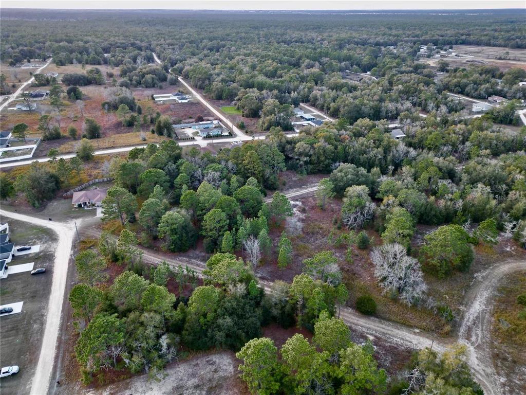 An aerial view shows a wooded lot with dirt roads and scattered houses nearby — TBD SW 145TH CT, OCALA, FL