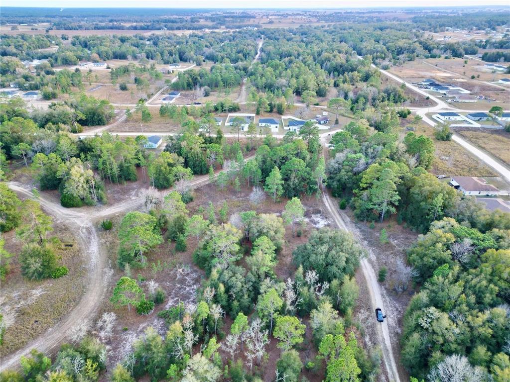 An aerial view shows a wooded lot with dirt roads and scattered houses in the distance — TBD SW 145TH CT, OCALA, FL