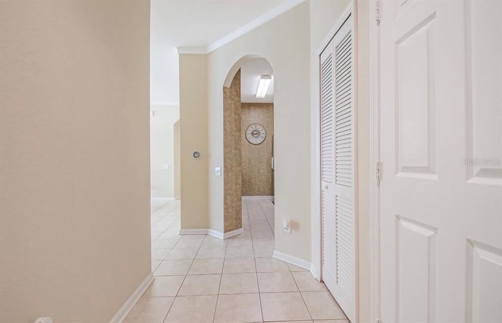 A hallway with tiled floors leads to an arched entryway featuring textured wallpaper and lighting — 3190 DANTE DRIVE UNIT 109, ORLANDO, FL