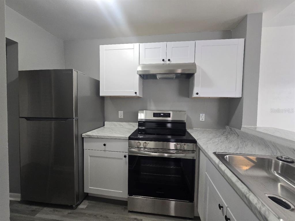 A kitchen features stainless steel appliances, white cabinets, and marble-patterned countertops — 5232 VIA HACIENDA CIRCLE UNIT A217, ORLANDO, FL