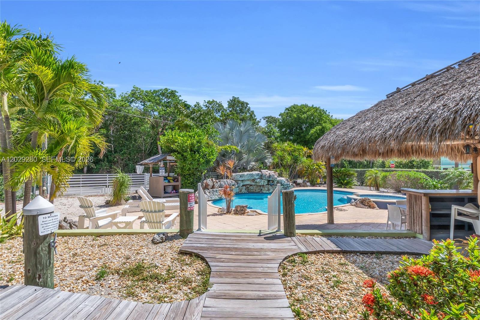 An outdoor pool area features a tiki hut, wooden walkway, and lush tropical landscaping — 443 4TH Rd, Key Largo FL 33037, KEY LARGO, FL