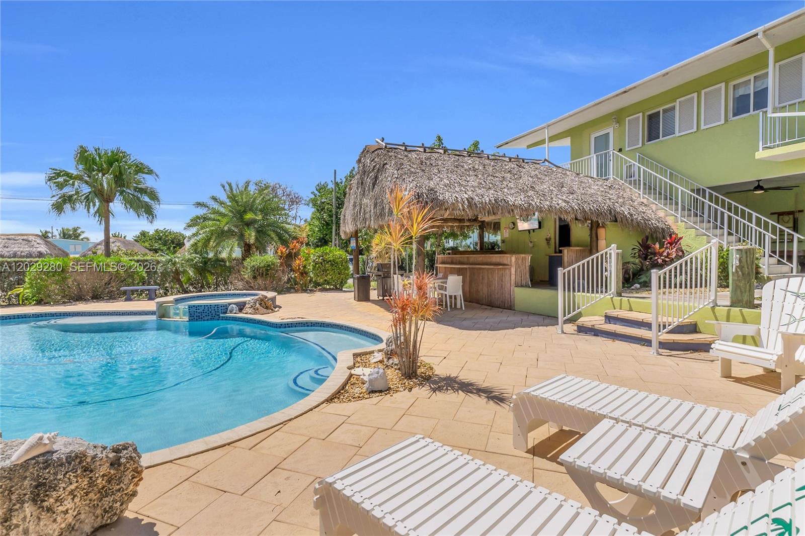 A swimming pool sits beside a thatched-roof tiki bar and a light green building — 443 4TH Rd, Key Largo FL 33037, KEY LARGO, FL