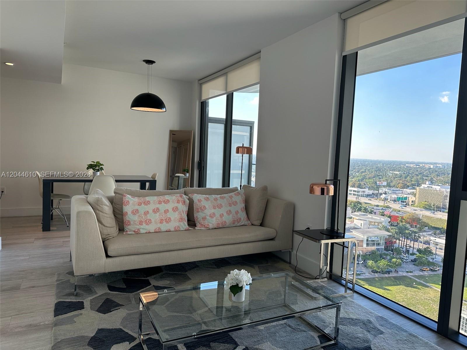 A modern living room features a beige sofa, glass coffee table, and floor-to-ceiling windows — 121 NE 34th St # 1915, Miami FL 33137, MIAMI, FL
