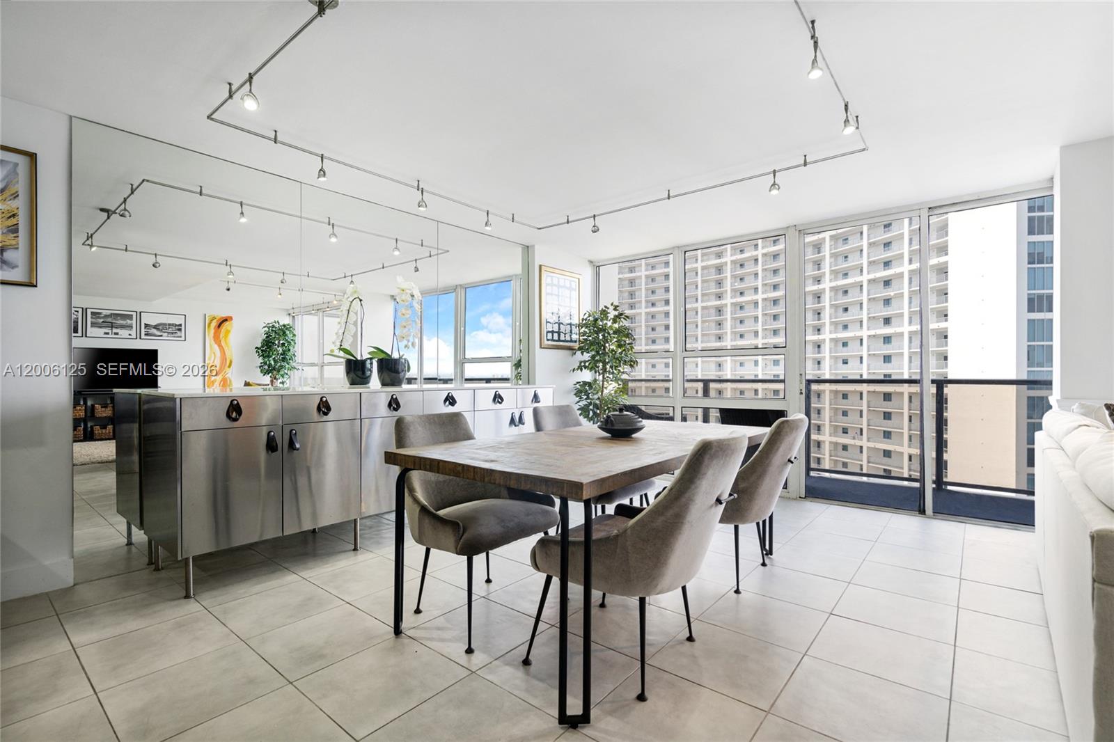 A dining room features a wooden table, grey chairs, stainless steel cabinetry, and floor-to-ceiling windows — 600 NE 36th St, Miami FL 33137, MIAMI, FL