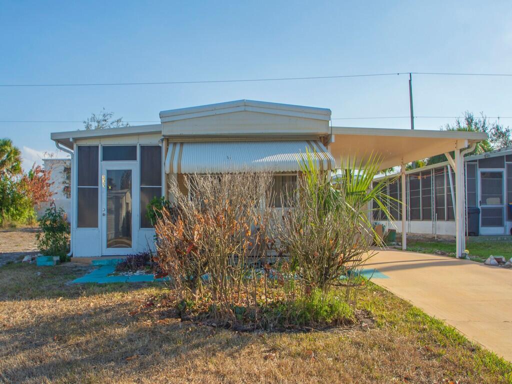 A single-story mobile home with a screened-in porch, metal awning, and an attached carport — 335 NE Tropicalia Lane, Jensen Beach FL 34957, JENSEN BEACH, FL