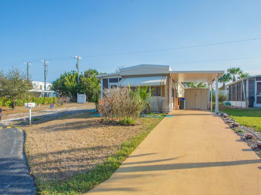 A mobile home with a tan driveway, carport, and storage shed under a blue sky — 335 NE Tropicalia Lane, Jensen Beach FL 34957, JENSEN BEACH, FL