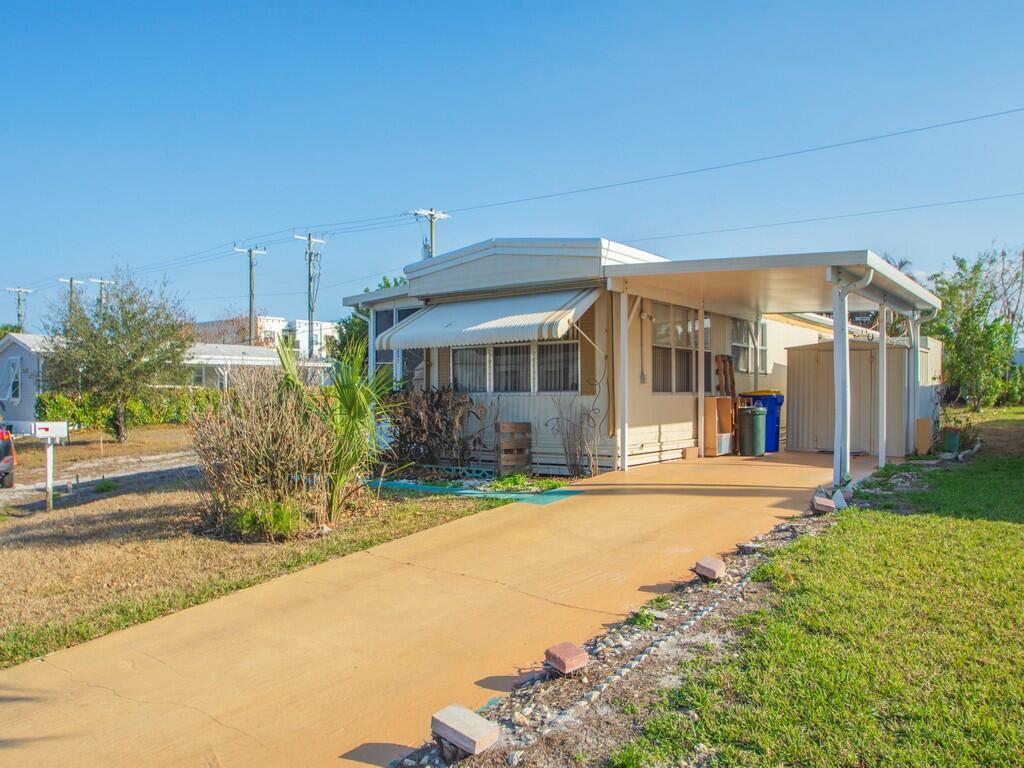 A single-story manufactured home with a carport, driveway, and small front yard — 335 NE Tropicalia Lane, Jensen Beach FL 34957, JENSEN BEACH, FL