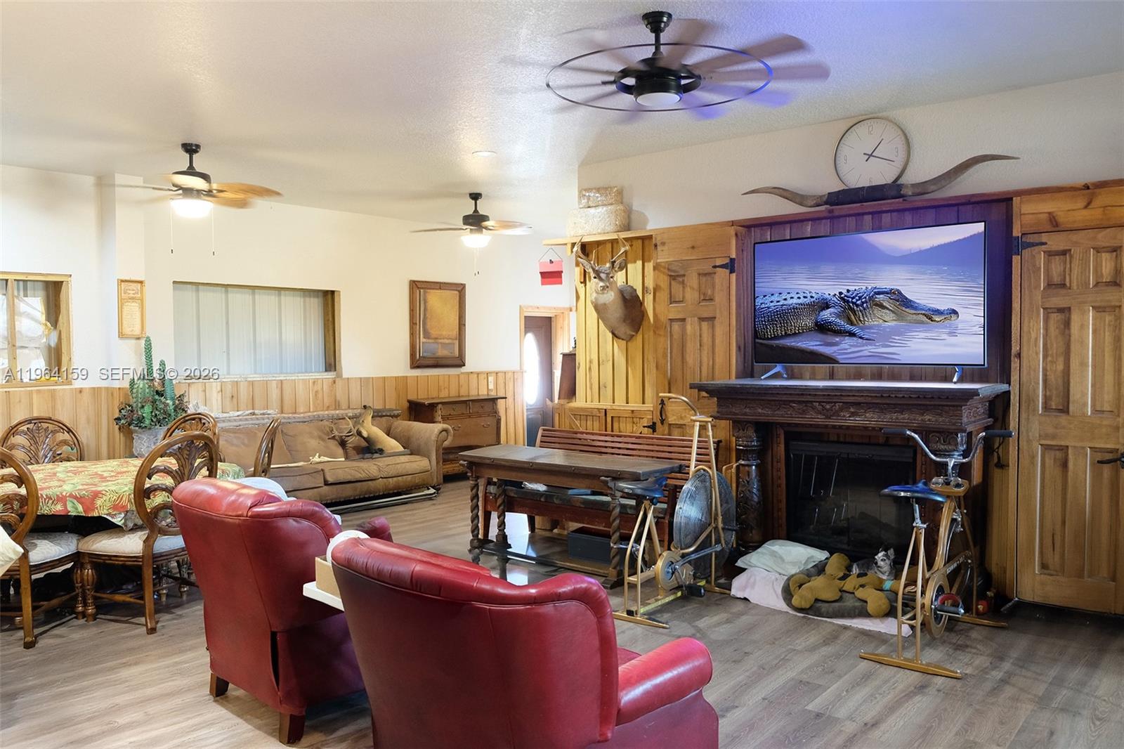 A rustic living room features wood paneling, a fireplace with a television, and red armchairs — 5271 US HWY 441 SE, Okeechobee FL 34974, OKEECHOBEE, FL