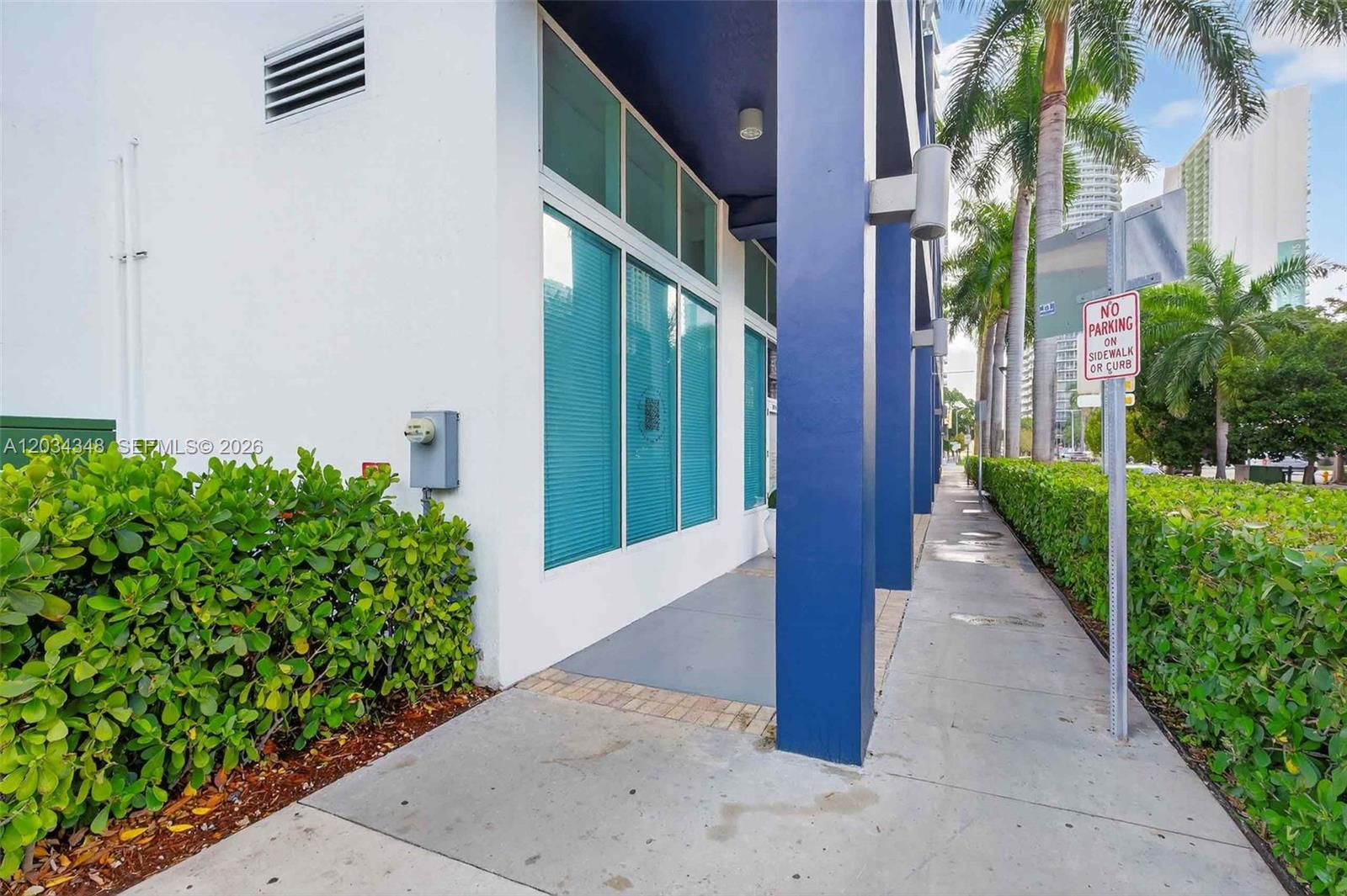 A sidewalk runs alongside a white building with blue columns and large glass windows — 275 NE 18th St, Miami FL 33132, MIAMI, FL