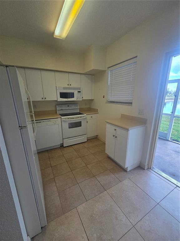A kitchen features white cabinetry, white appliances, tan countertops, and tile flooring near a patio — 8312 BERNWOOD COVE LOOP UNIT 1007, FORT MYERS, FL