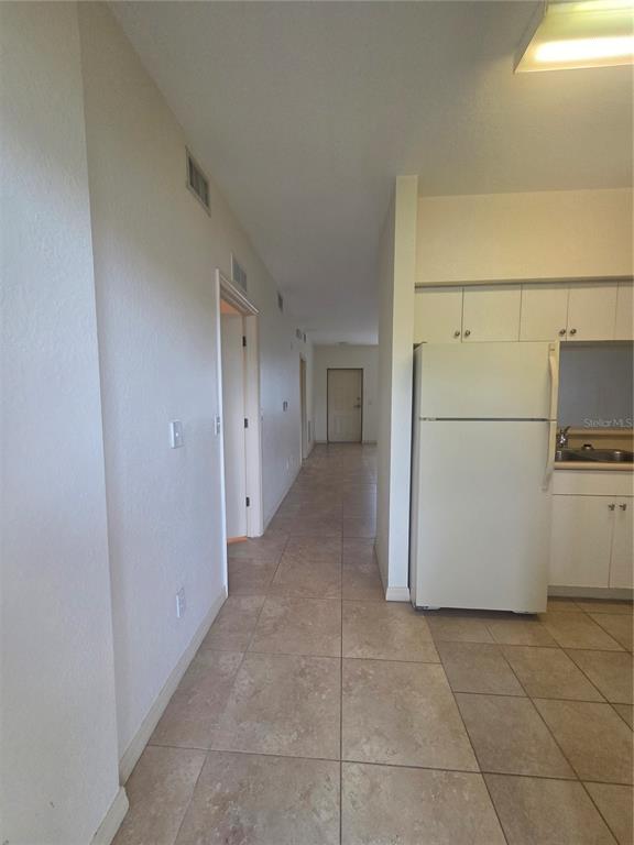A hallway leads to a closed door, with a kitchen featuring white cabinets and appliances — 8312 BERNWOOD COVE LOOP UNIT 1007, FORT MYERS, FL