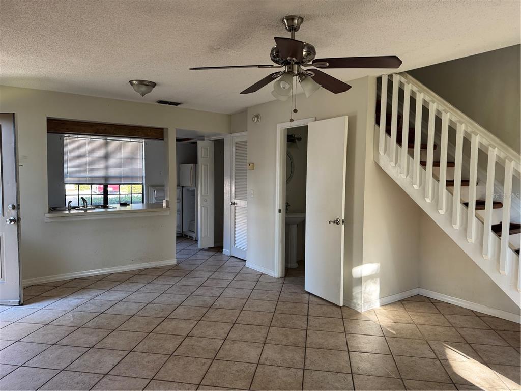 A room with tiled floors, a ceiling fan, a staircase, and an open kitchen pass-through — 16573 BRIGADOON DRIVE, TAMPA, FL