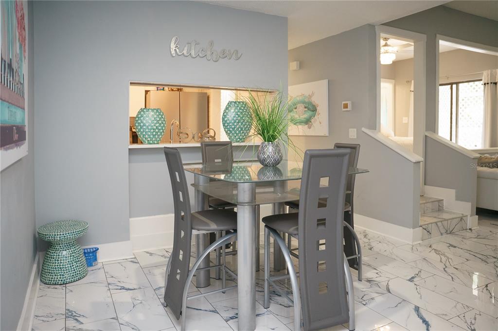 A dining area features a glass-topped table, gray chairs, and white marble-look tile flooring — 4405 W FAIR OAKS AVENUE UNIT 2, TAMPA, FL