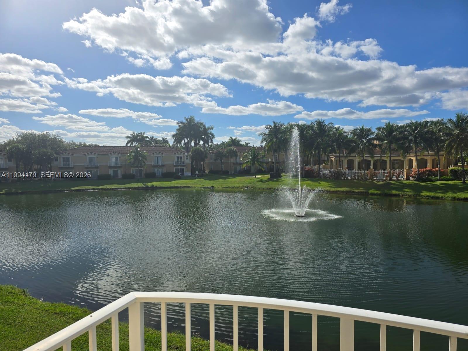 A view from a balcony overlooking a pond with a fountain and residential buildings — 3076 SW 129th Ave # 152, Miramar FL 33027, MIRAMAR, FL