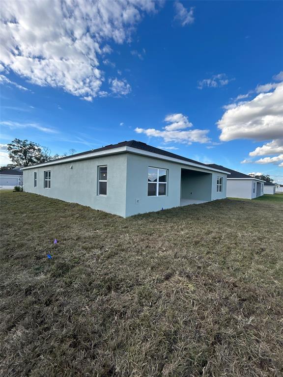 The exterior of a light green stucco house with a covered patio and dark roof — 10918 SW 72ND CIRCLE, OCALA, FL