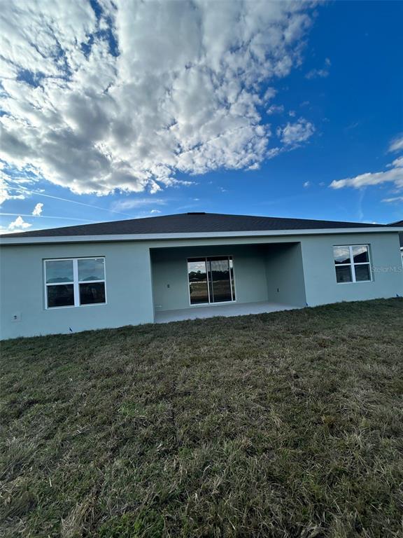 The exterior rear view of a single-story house features a covered patio and lawn — 10918 SW 72ND CIRCLE, OCALA, FL