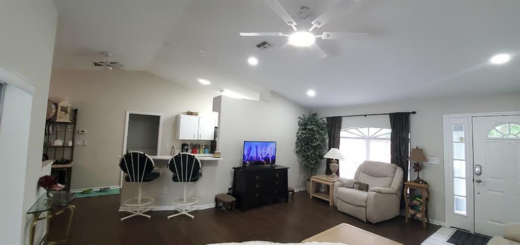A living room with dark wood floors, a ceiling fan, a television, and a kitchen bar — 2534 N BRENTWOOD CIRCLE, LECANTO, FL