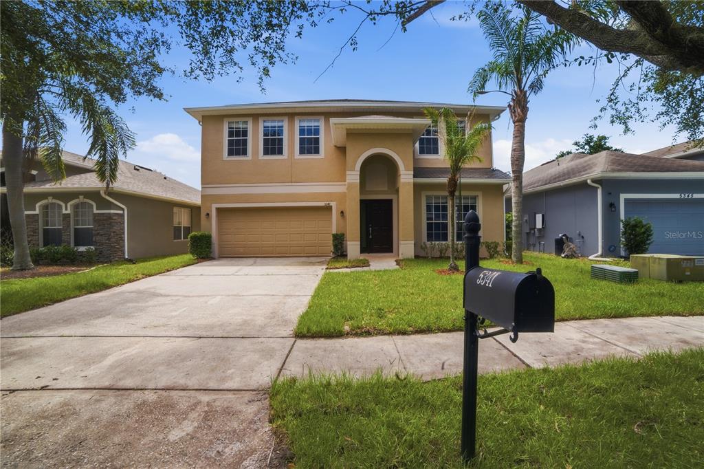 A two-story tan house with a two-car garage and a front lawn — 5341 PEPPER BRUSH COVE, APOPKA, FL