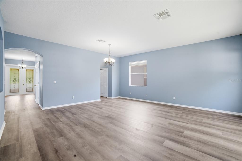An empty room with light blue walls, wood-look flooring, and a central chandelier — 5341 PEPPER BRUSH COVE, APOPKA, FL