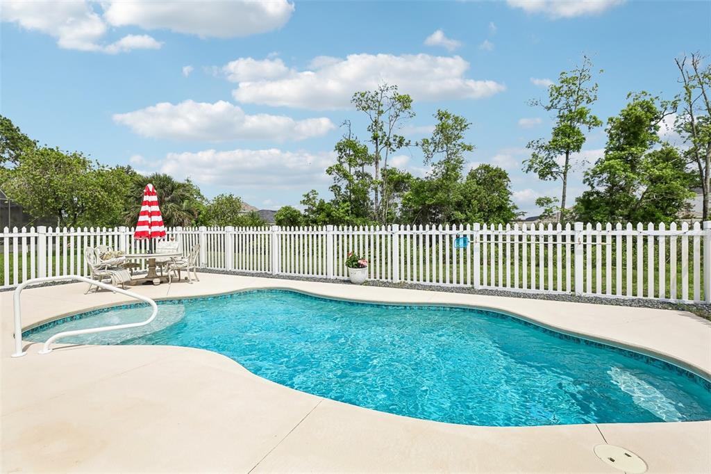 A backyard swimming pool with a white picket fence and patio furniture under an umbrella — 60 WOODBURY DRIVE, PALM COAST, FL