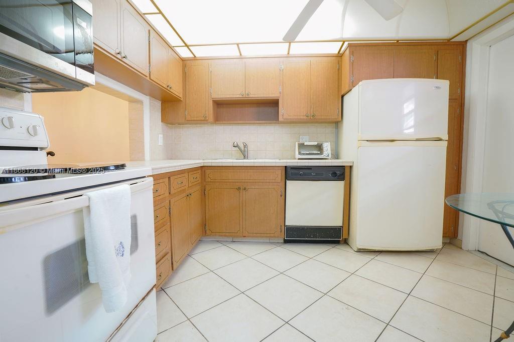 This kitchen features light wood cabinets, white appliances, and light-colored tile flooring — 215 SE 3rd Ave # 401D, Hallandale Beach FL 33009, HALLANDALE BEACH, FL