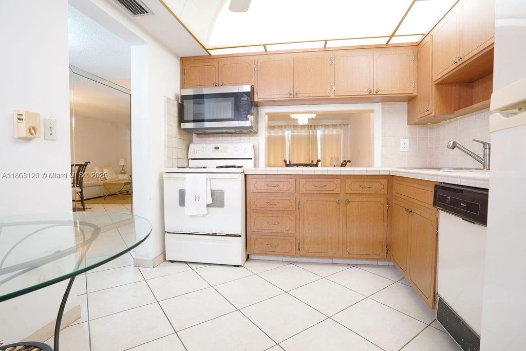 This kitchen features light wood cabinets, white appliances, a tiled floor, and a pass-through window — 215 SE 3rd Ave # 401D, Hallandale Beach FL 33009, HALLANDALE BEACH, FL