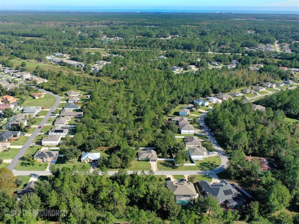 An aerial view shows a suburban neighborhood surrounded by dense forest with the ocean visible — 37 LEIGHTON LANE, PALM COAST, FL