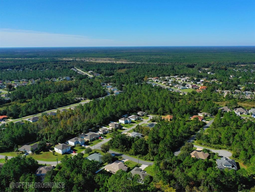 An aerial view shows a suburban neighborhood surrounded by dense forest under a clear sky — 37 LEIGHTON LANE, PALM COAST, FL