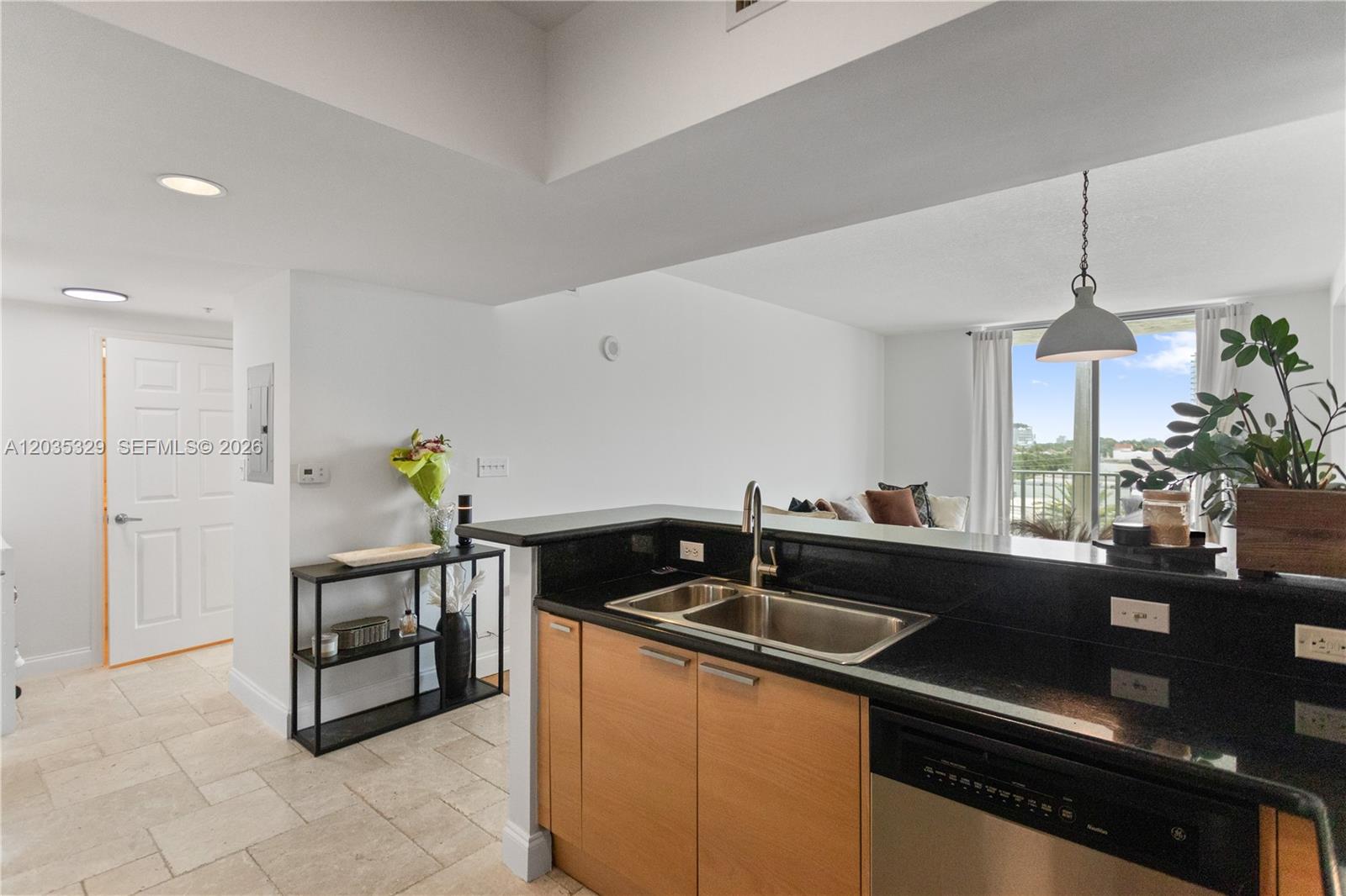 A kitchen with black countertops and light wood cabinets overlooks a living area with balcony access — 140 S Dixie Hwy # 417, Hollywood FL 33020, HOLLYWOOD, FL