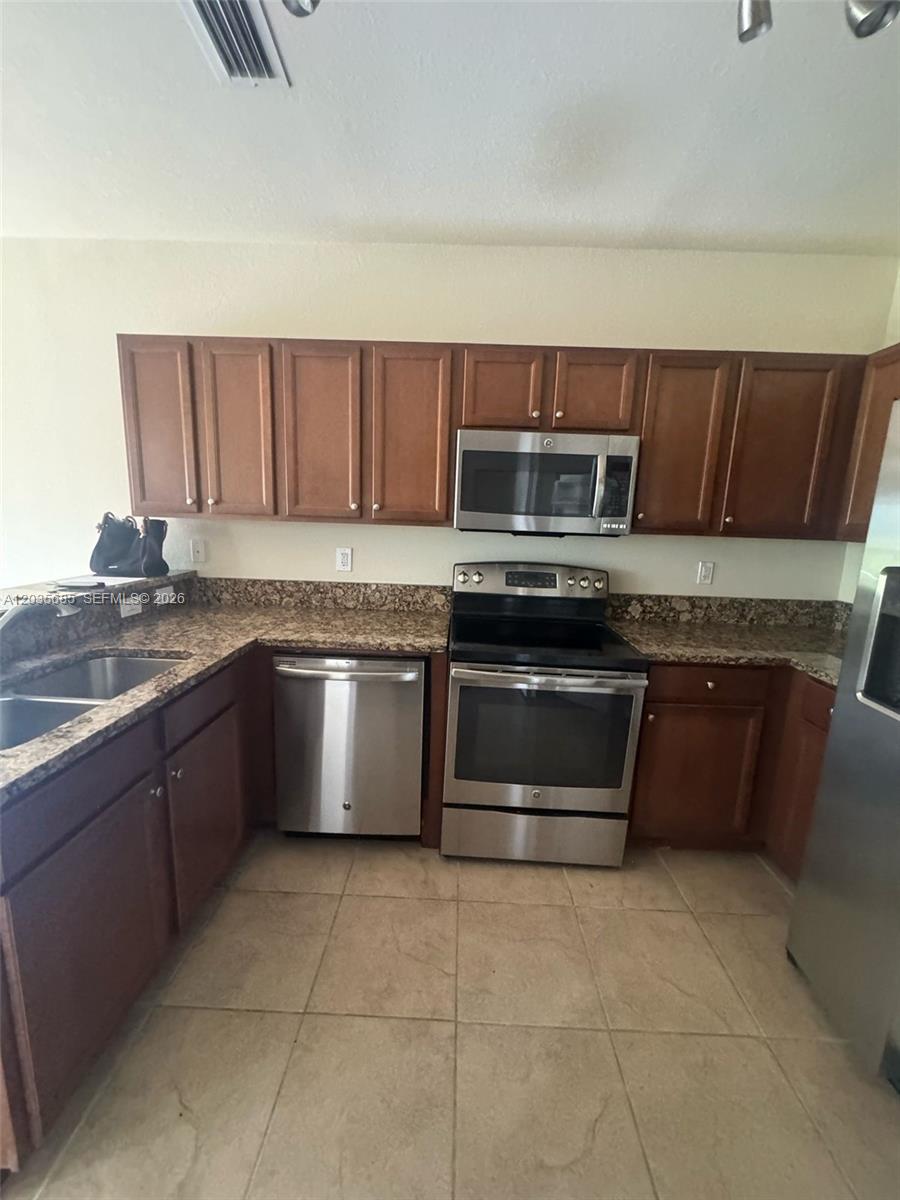 A kitchen features wood cabinets, granite countertops, and stainless steel appliances over tile flooring — 8900 NW 97th Ave # 212, Doral FL 33178, DORAL, FL