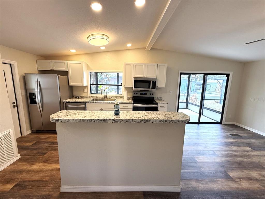 A kitchen features white cabinets, stainless steel appliances, granite countertops, and wood-look flooring — 2055 S FLORAL AVENUE UNIT 214, BARTOW, FL