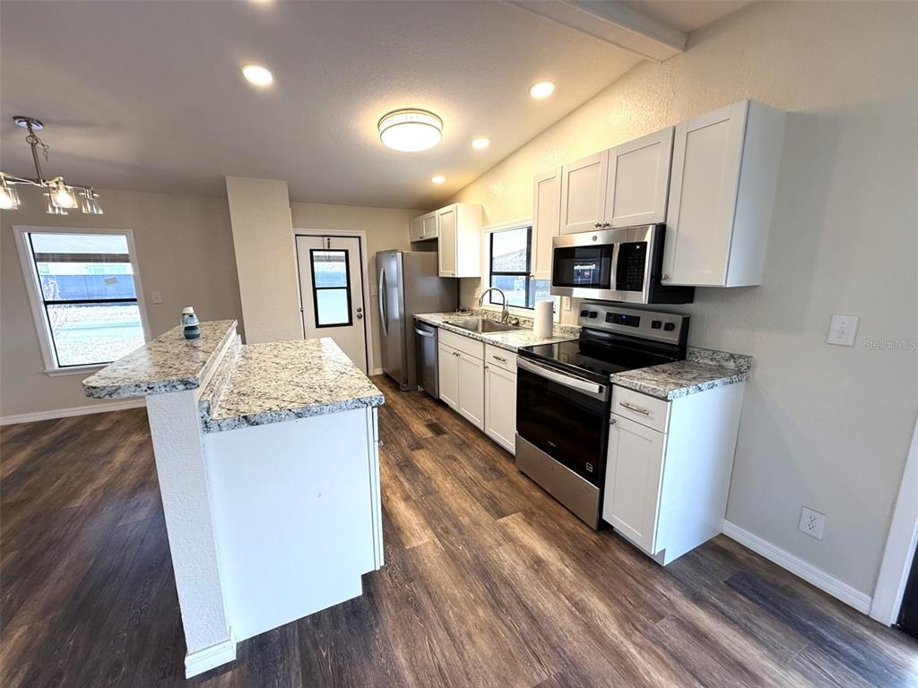 A kitchen features white cabinets, granite countertops, stainless steel appliances, and wood-look flooring — 2055 S FLORAL AVENUE UNIT 214, BARTOW, FL