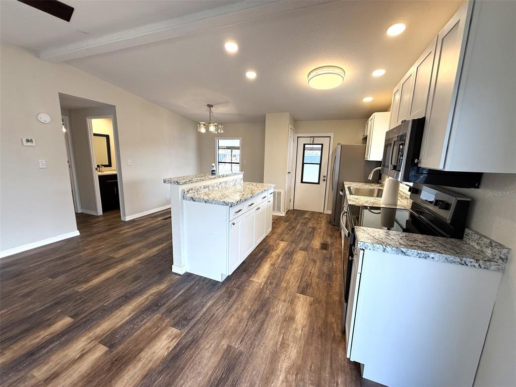 A kitchen with white cabinets, granite countertops, and wood-look flooring opens to a dining area — 2055 S FLORAL AVENUE UNIT 214, BARTOW, FL