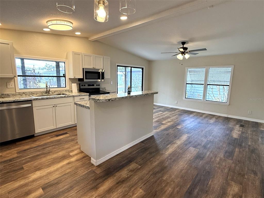 This kitchen and living area features white cabinets, granite countertops, and wood-look flooring — 2055 S FLORAL AVENUE UNIT 214, BARTOW, FL