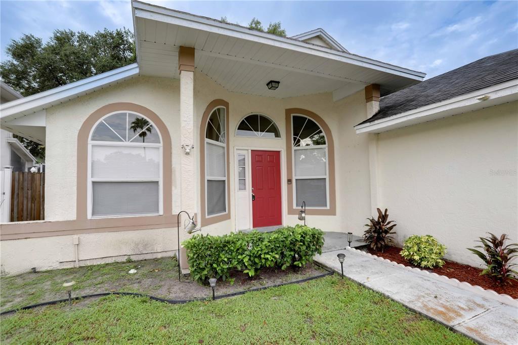 The exterior of a single-story house features a red front door and arched windows — 10038 LITTLE TEAK STREET, ORLANDO, FL