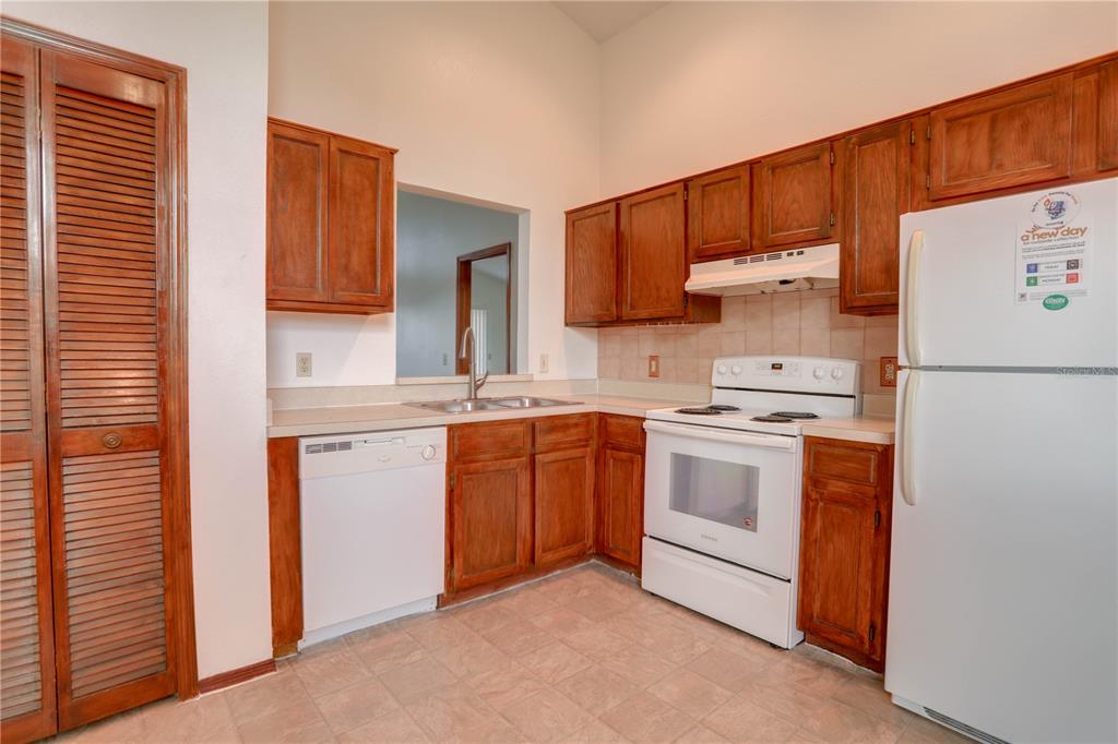 A kitchen with wood cabinets, white appliances, a double sink, and tiled flooring — 10038 LITTLE TEAK STREET, ORLANDO, FL