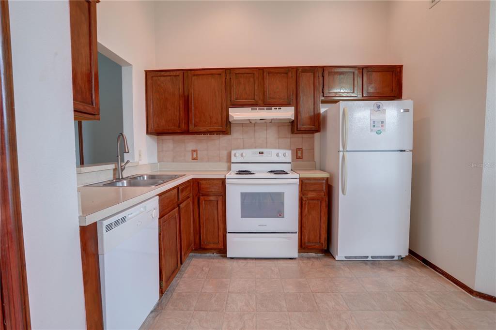 A kitchen features wood cabinets, white appliances, a double sink, and light-colored tile flooring — 10038 LITTLE TEAK STREET, ORLANDO, FL