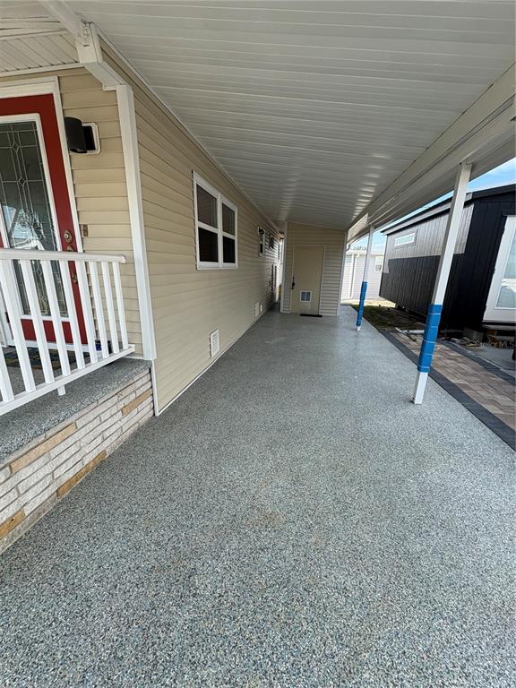 A covered carport with a speckled concrete floor runs alongside a tan mobile home — 1706 WISCONSIN AVENUE, BRADENTON, FL